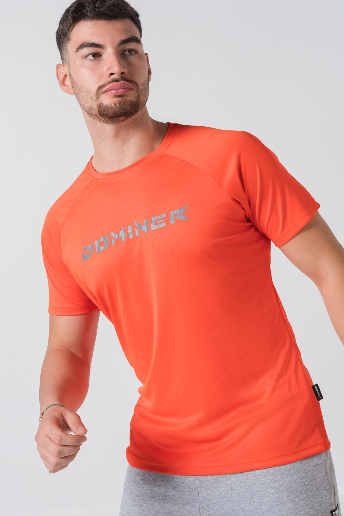 Casual t-shirt SHIFT – Bluzë sportive/casual me mëngë të shkurtra raglan për meshkuj në ngjyrë portokalli të ndezur (coral/orange), me jakë të rrumbullakët, emrin e markës Dominer të printuar në gjoks, logo minimale në pjesën e pasme sipër dhe etikete anësore.