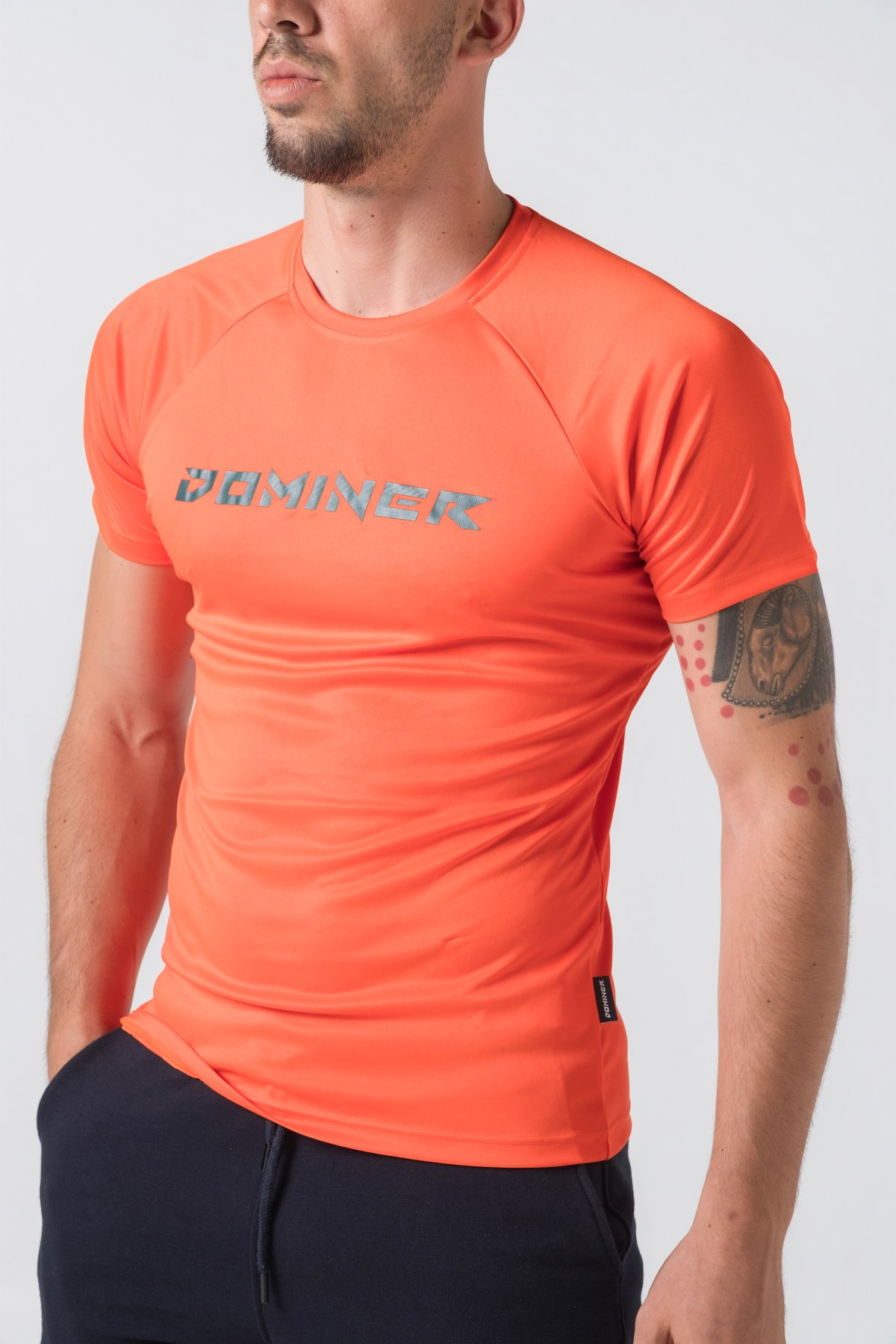 Casual t-shirt SHIFT – Bluzë sportive/casual me mëngë të shkurtra raglan për meshkuj në ngjyrë portokalli të ndezur (coral/orange), me jakë të rrumbullakët, emrin e markës Dominer të printuar në gjoks, logo minimale në pjesën e pasme sipër dhe etikete anësore.