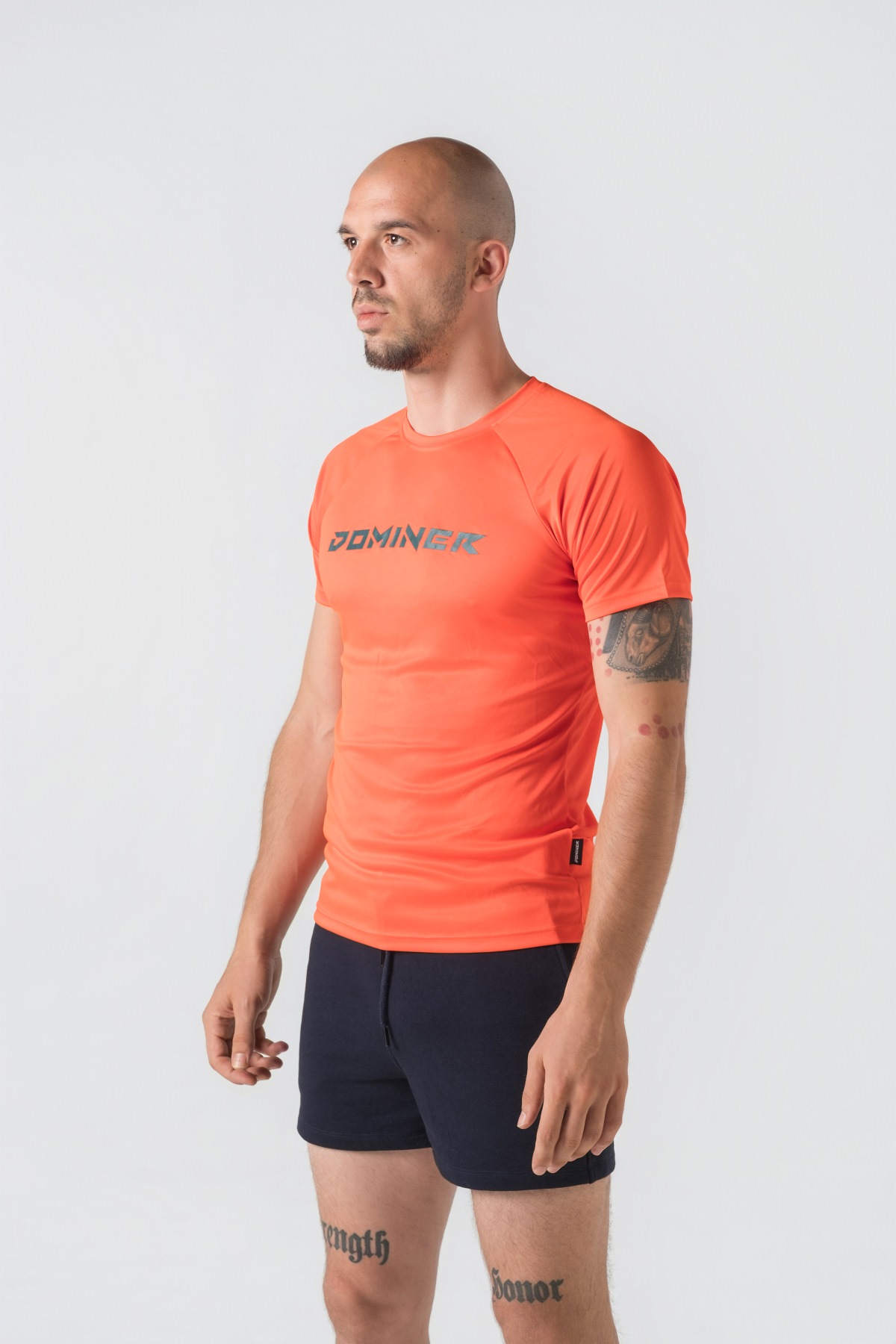 Casual t-shirt SHIFT – Bluzë sportive/casual me mëngë të shkurtra raglan për meshkuj në ngjyrë portokalli të ndezur (coral/orange), me jakë të rrumbullakët, emrin e markës Dominer të printuar në gjoks, logo minimale në pjesën e pasme sipër dhe etikete anësore.