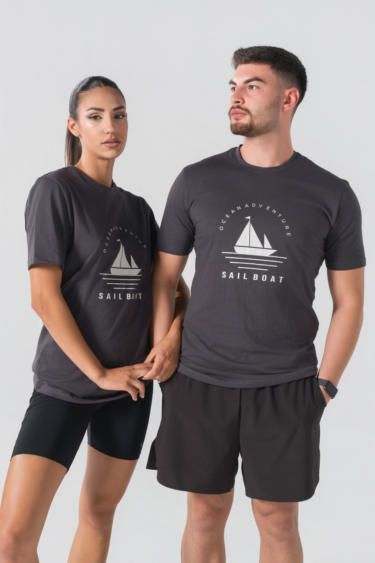 T-shirt Breezy Unisex – Bluzë e thjeshtë me mëngë të shkurtra unisex në ngjyrë hiri të mbyllur (dark grey/charcoal), me jakë të rrumbullakët, print grafik veror detar me anije me vela dhe mbishkrimin "Ocean Adventure / Sail Boat" në ngjyrë të bardhë në gjoks.
