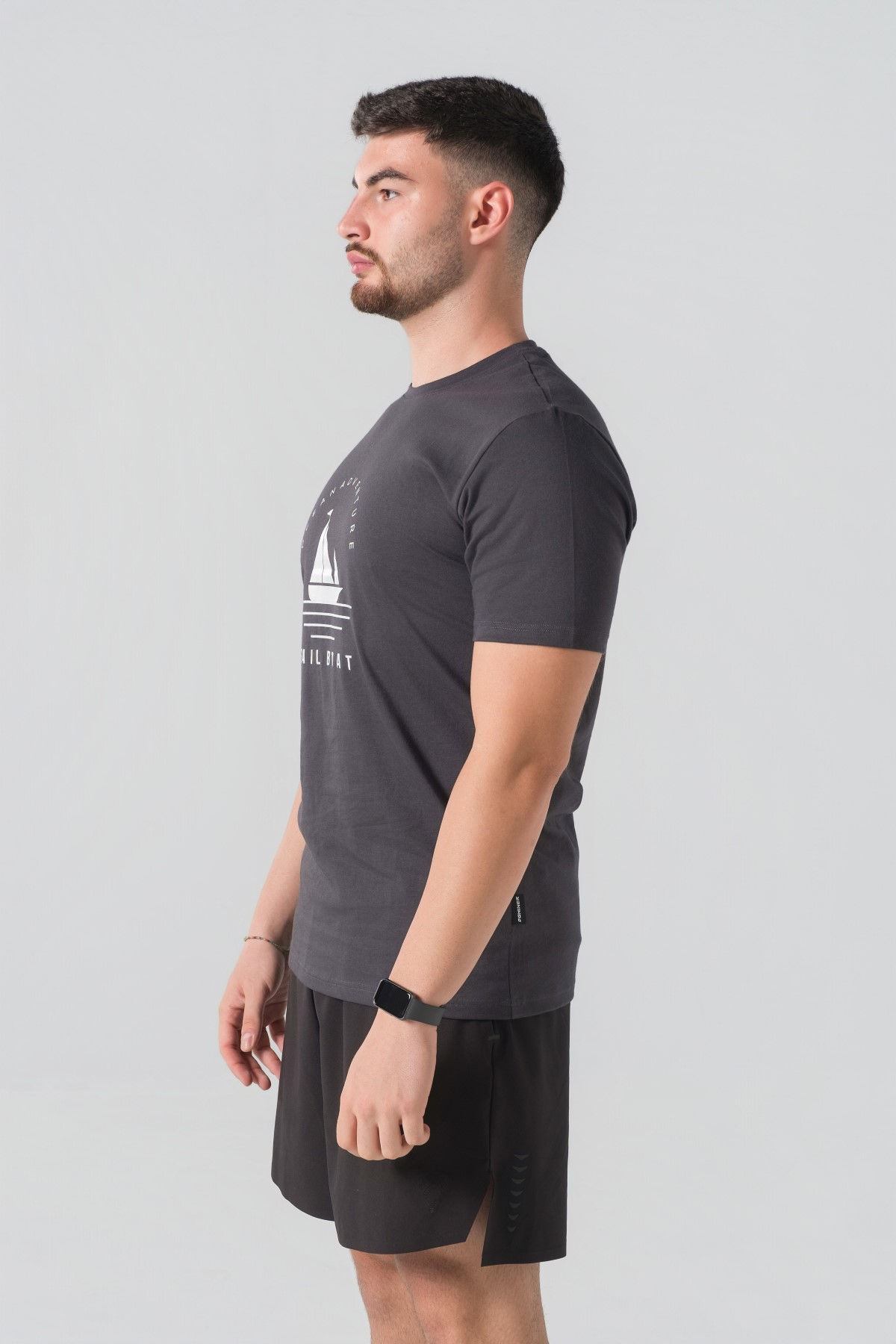 T-shirt Breezy Unisex – Bluzë e thjeshtë me mëngë të shkurtra unisex në ngjyrë hiri të mbyllur (dark grey/charcoal), me jakë të rrumbullakët, print grafik veror detar me anije me vela dhe mbishkrimin "Ocean Adventure / Sail Boat" në ngjyrë të bardhë në gjoks.