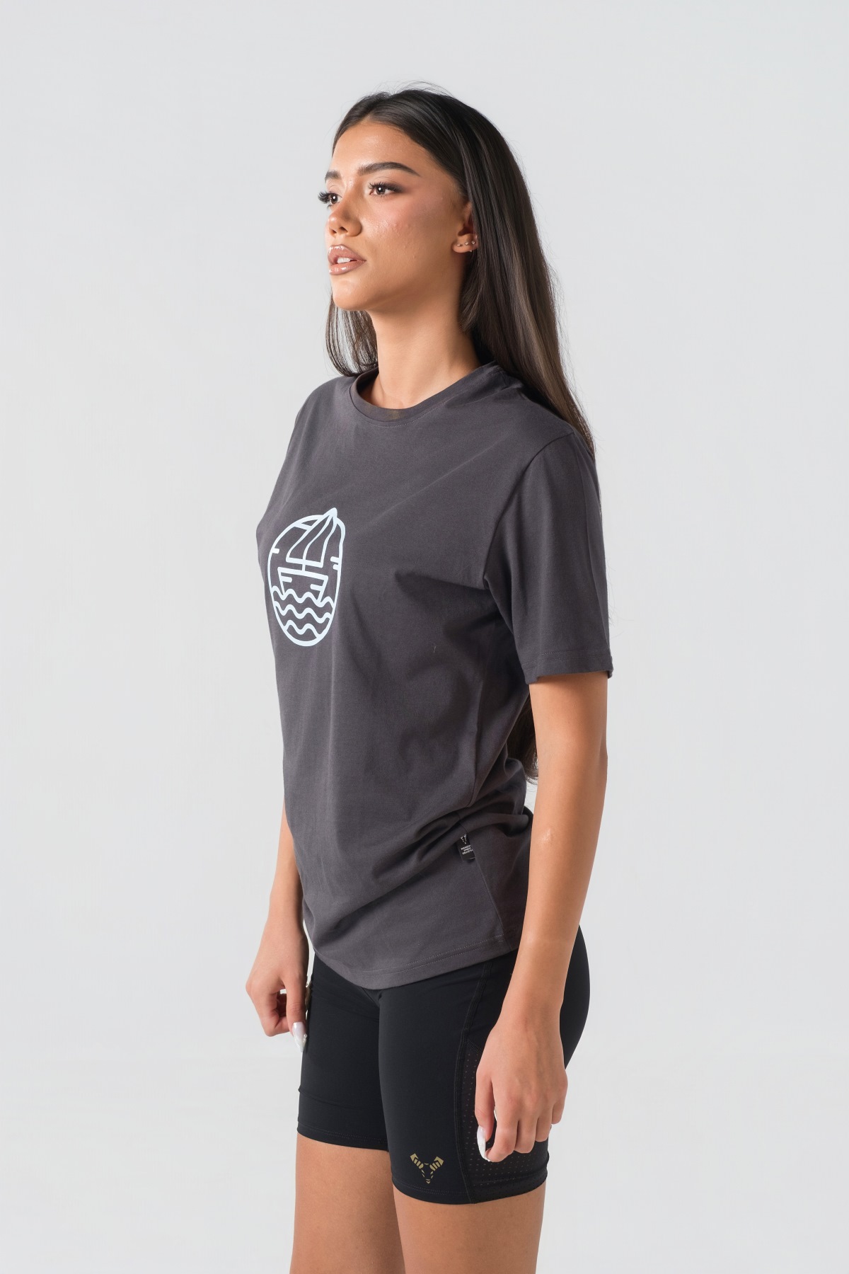 T-shirt Breezy Unisex – Bluzë e thjeshtë me mëngë të shkurtra unisex në ngjyrë hiri të mbyllur (dark grey/charcoal), me jakë të rrumbullakët, print grafik me emblemë rrethore detare me anije/varkë dhe valë deti në ngjyrë të kaltër të çelët në gjoks.
