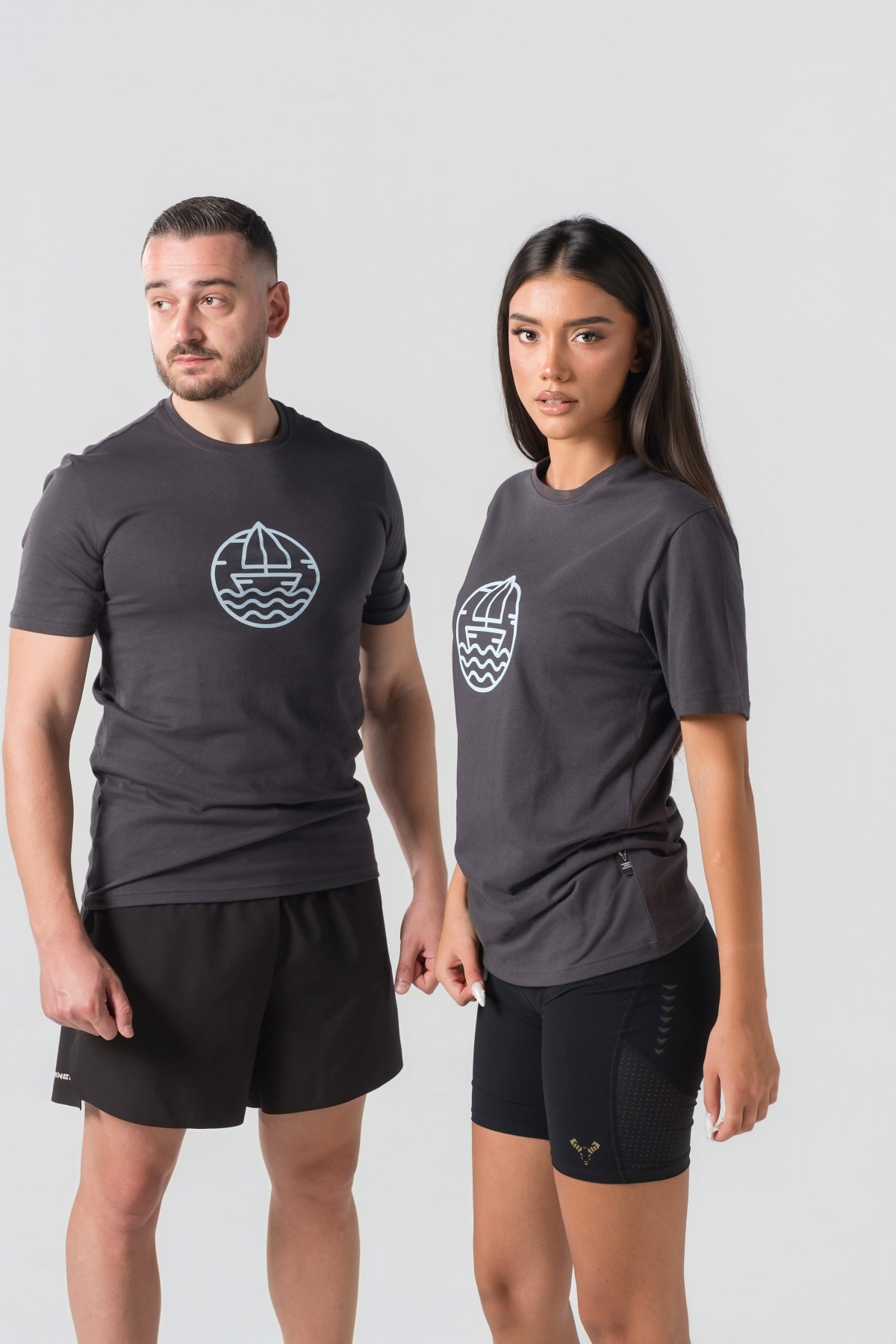 T-shirt Breezy Unisex – Bluzë e thjeshtë me mëngë të shkurtra unisex në ngjyrë hiri të mbyllur (dark grey/charcoal), me jakë të rrumbullakët, print grafik me emblemë rrethore detare me anije/varkë dhe valë deti në ngjyrë të kaltër të çelët në gjoks.