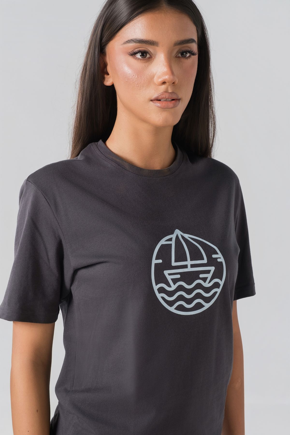 T-shirt Breezy Unisex – Bluzë e thjeshtë me mëngë të shkurtra unisex në ngjyrë hiri të mbyllur (dark grey/charcoal), me jakë të rrumbullakët, print grafik me emblemë rrethore detare me anije/varkë dhe valë deti në ngjyrë të kaltër të çelët në gjoks.