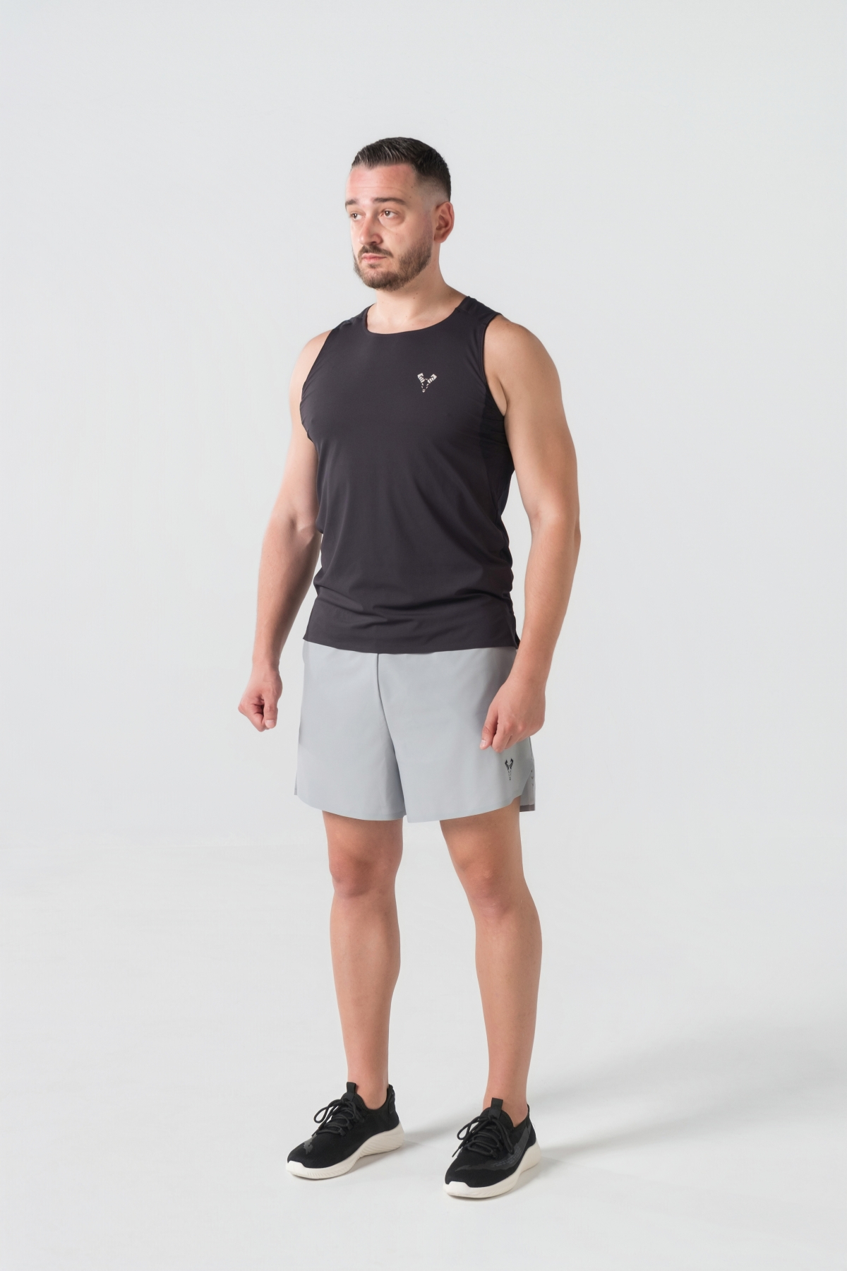 Shift Kanatjere Meshkujsh – Kanatjere sportive për meshkuj në ngjyrë të zezë, me jakë të rrumbullakët, material me teksturë rrjetë (mesh) në shpinë për ajrosje, të çara të vogla anësore në fund, logo minimale Dominer në gjoks, emrin e markës të printuar në pjesën e pasme sipër dhe detaj vertikal me shigjeta në pjesën e poshtme prapa.