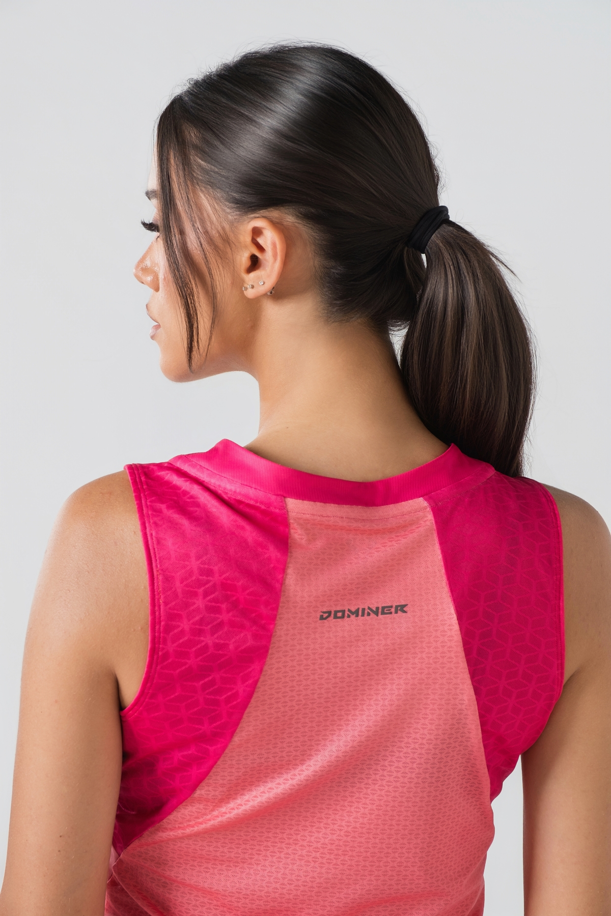 Shift Kanatjere Femrash – Kanatjere sportive për femra në ngjyrë rozë të çelët (coral pink) me panela anësore dhe në shpatulla në ngjyrë rozë më të mbyllur (fuchsia), jakë të rrumbullakët, panel rrjetë (mesh) të shpuar në shpinë për ajrosje, të çara të vogla anësore në fund, logo minimale Dominer në gjoks dhe emrin e markës të printuar në pjesën e pasme sipër.