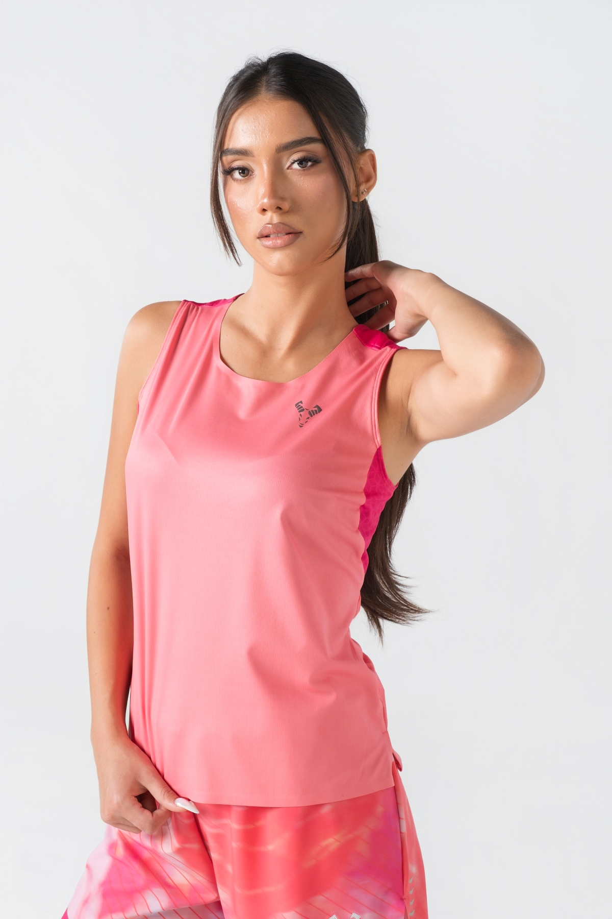 Shift Kanatjere Femrash – Kanatjere sportive për femra në ngjyrë rozë të çelët (coral pink) me panela anësore dhe në shpatulla në ngjyrë rozë më të mbyllur (fuchsia), jakë të rrumbullakët, panel rrjetë (mesh) të shpuar në shpinë për ajrosje, të çara të vogla anësore në fund, logo minimale Dominer në gjoks dhe emrin e markës të printuar në pjesën e pasme sipër.