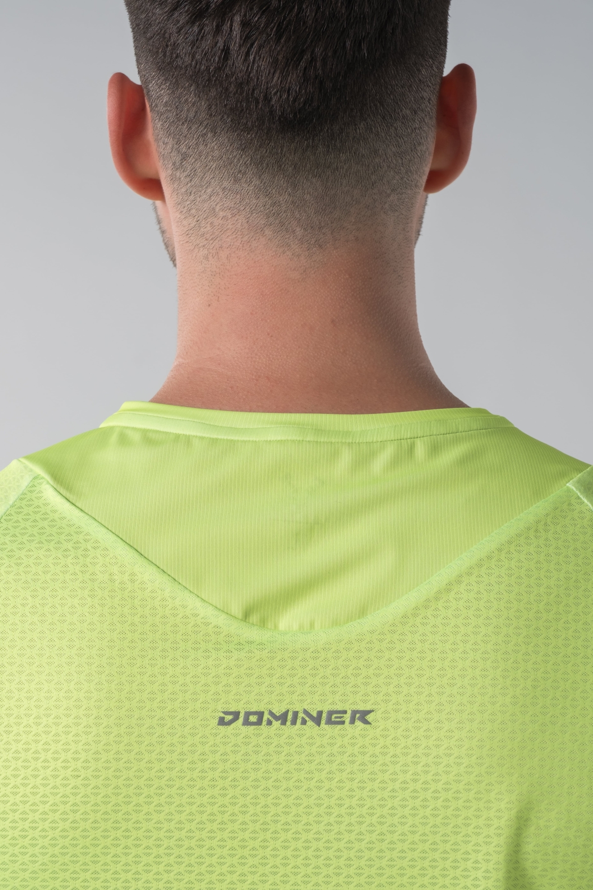 Shift Bluze Meshkujsh – Bluzë sportive me mëngë të shkurtra për meshkuj në ngjyrë të verdhë me neoni (lime green/yellow), me jakë të rrumbullakët, material me teksturë rrjetë (mesh) prapa dhe në mëngë për ajrosje, të çara të vogla anësore në fund, logo minimale Dominer në gjoks dhe emrin e markës të printuar në pjesën e pasme sipër.