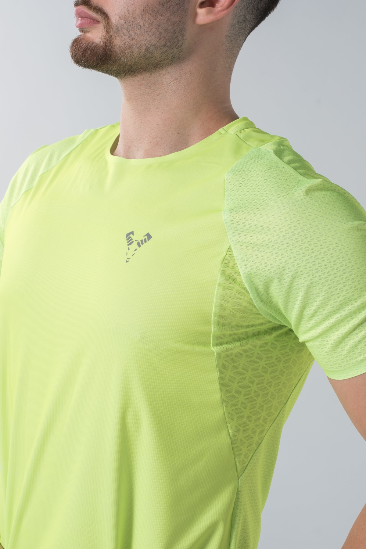 Shift Bluze Meshkujsh – Bluzë sportive me mëngë të shkurtra për meshkuj në ngjyrë të verdhë me neoni (lime green/yellow), me jakë të rrumbullakët, material me teksturë rrjetë (mesh) prapa dhe në mëngë për ajrosje, të çara të vogla anësore në fund, logo minimale Dominer në gjoks dhe emrin e markës të printuar në pjesën e pasme sipër.