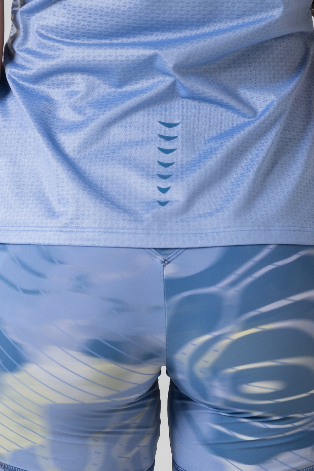 Shift Bluze Femrash – Bluzë sportive me mëngë të shkurtra për femra në ngjyrë të kaltër, me jakë të rrumbullakët me detaj të verdhë pastel, material me teksturë rrjetë (mesh) në shpinë, mëngë dhe panela anësore për ajrosje, të çara të vogla anësore në fund, logo minimale Dominer në gjoks, emrin e markës të printuar në pjesën e pasme sipër dhe detaj vertikal me shigjeta në pjesën e poshtme prapa.