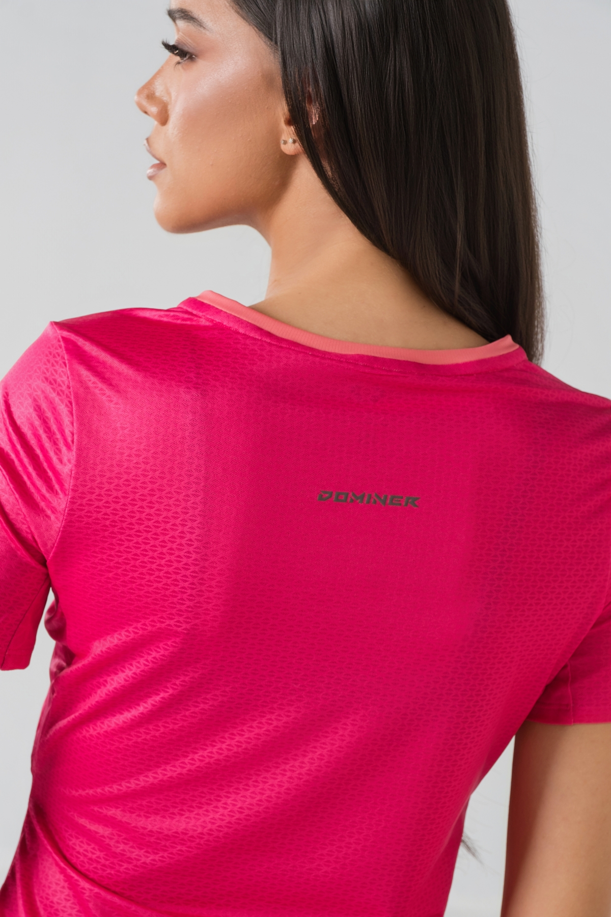 Shift Bluze Femrash – Bluzë sportive me mëngë të shkurtra për femra në ngjyrë rozë elektrike (pink/fuchsia), me jakë të rrumbullakët me detaj rozë më të çelët, material me teksturë rrjetë (mesh) në shpinë, mëngë dhe panela anësore për ajrosje, të çara të vogla anësore në fund, logo minimale Dominer në gjoks dhe emrin e markës të printuar në pjesën e pasme sipër.