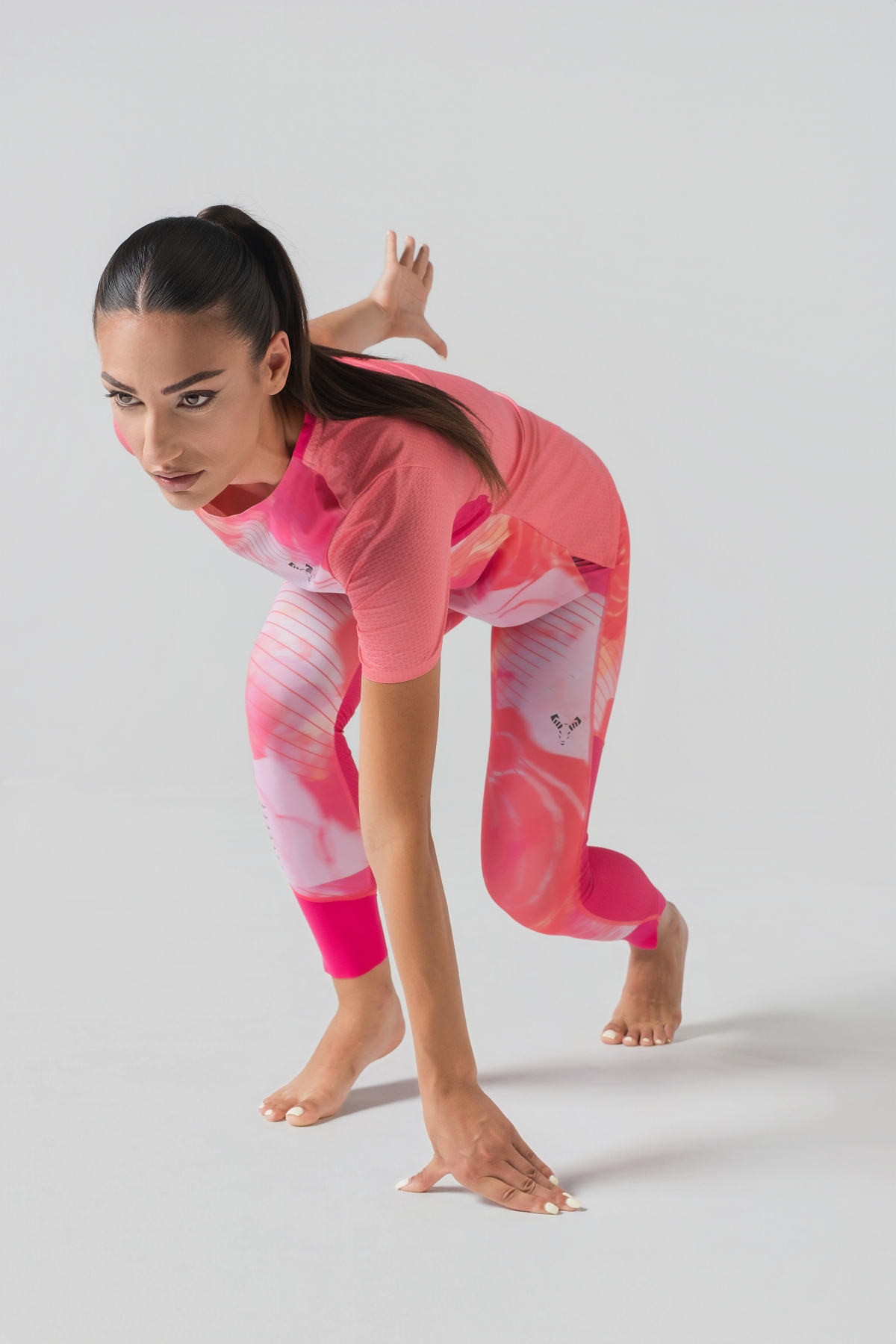 Shift Bluze Femrash – Bluzë sportive me mëngë të shkurtra për femra me print grafik abstrakt/mermer me motiv trëndafili në nuanca të rozës (pink, fuchsia, coral), me jakë të rrumbullakët, material me teksturë rrjetë (mesh) në shpinë, mëngë dhe panela anësore për ajrosje, të çara të vogla anësore në fund, logo minimale Dominer në gjoks dhe emrin e markës të printuar në pjesën e pasme sipër.