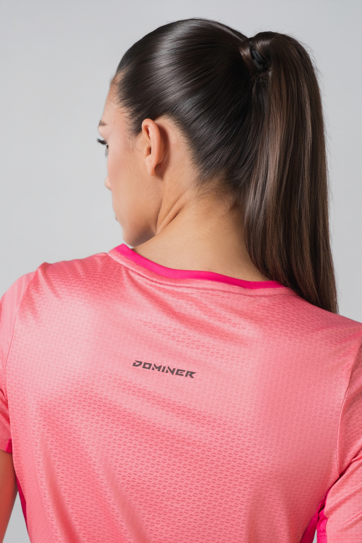 Shift Bluze Femrash – Bluzë sportive me mëngë të shkurtra për femra me print grafik abstrakt/mermer me motiv trëndafili në nuanca të rozës (pink, fuchsia, coral), me jakë të rrumbullakët, material me teksturë rrjetë (mesh) në shpinë, mëngë dhe panela anësore për ajrosje, të çara të vogla anësore në fund, logo minimale Dominer në gjoks dhe emrin e markës të printuar në pjesën e pasme sipër.