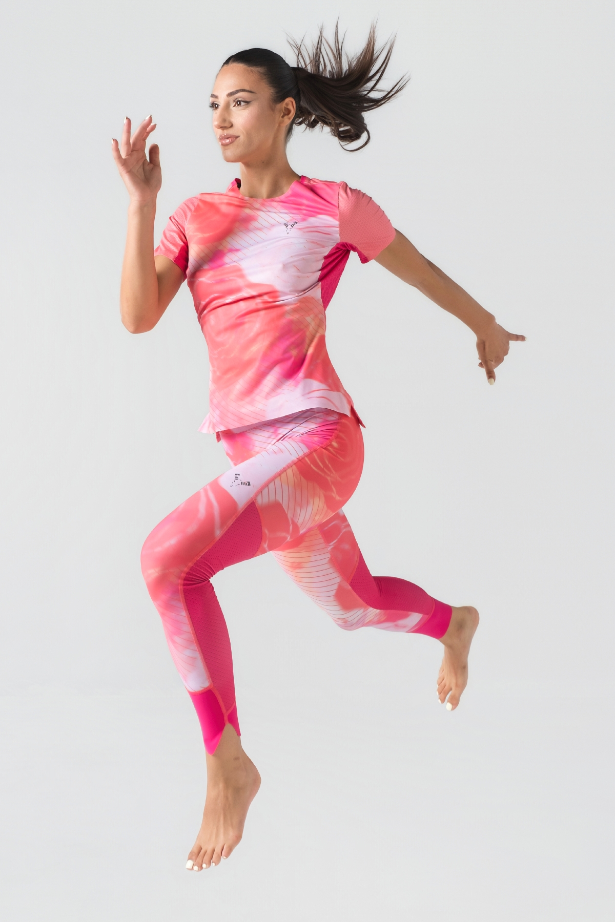 Shift Bluze Femrash – Bluzë sportive me mëngë të shkurtra për femra me print grafik abstrakt/mermer me motiv trëndafili në nuanca të rozës (pink, fuchsia, coral), me jakë të rrumbullakët, material me teksturë rrjetë (mesh) në shpinë, mëngë dhe panela anësore për ajrosje, të çara të vogla anësore në fund, logo minimale Dominer në gjoks dhe emrin e markës të printuar në pjesën e pasme sipër.