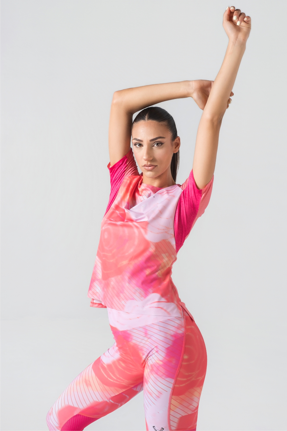 Shift Bluze Femrash – Bluzë sportive me mëngë të shkurtra për femra me print grafik abstrakt/mermer me motiv trëndafili në nuanca të rozës (pink, fuchsia, coral), me jakë të rrumbullakët, material me teksturë rrjetë (mesh) në shpinë, mëngë dhe panela anësore për ajrosje, të çara të vogla anësore në fund, logo minimale Dominer në gjoks dhe emrin e markës të printuar në pjesën e pasme sipër.