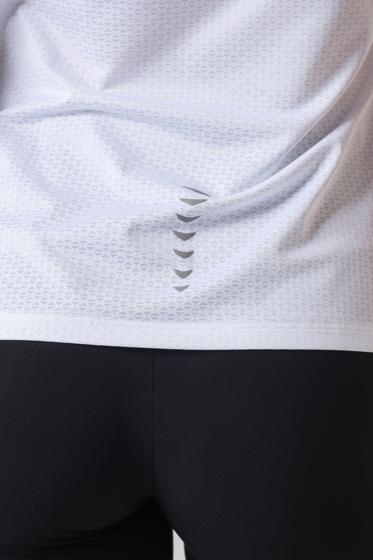 Shift Bluze Femrash – Bluzë sportive me mëngë të shkurtra për femra në ngjyrë të bardhë, me jakë të rrumbullakët, material me teksturë rrjetë (mesh) në shpinë, mëngë dhe panela anësore për ajrosje, të çara të vogla anësore në fund, logo minimale Dominer në gjoks dhe detaj vertikal me shigjeta në pjesën e poshtme prapa.
