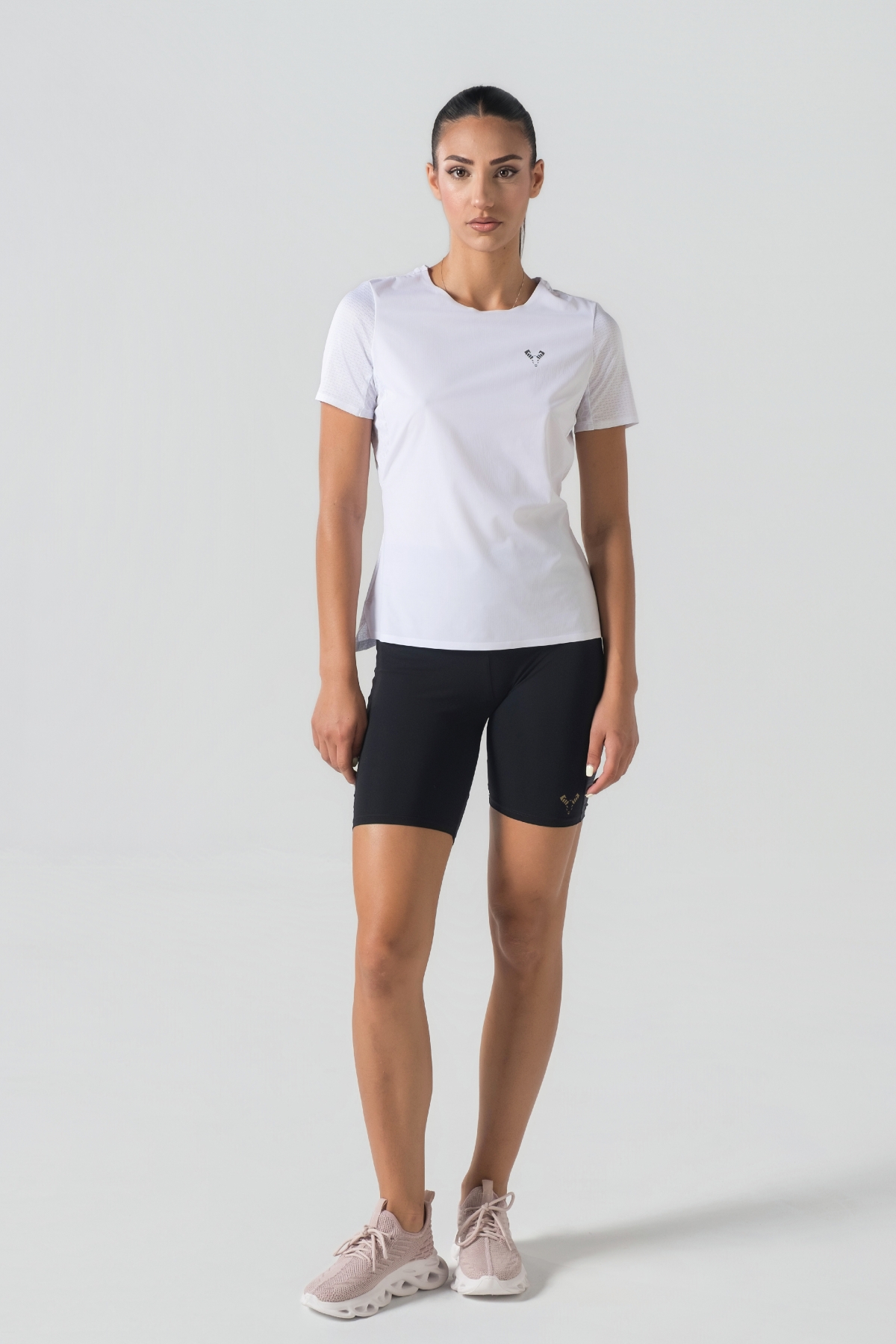 Shift Bluze Femrash – Bluzë sportive me mëngë të shkurtra për femra në ngjyrë të bardhë, me jakë të rrumbullakët, material me teksturë rrjetë (mesh) në shpinë, mëngë dhe panela anësore për ajrosje, të çara të vogla anësore në fund, logo minimale Dominer në gjoks dhe detaj vertikal me shigjeta në pjesën e poshtme prapa.
